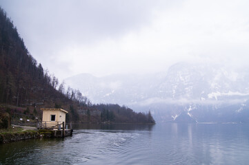 Fototapeta premium Tiny harbor on the Hallstatt Lake in the middle of the Alps, mountains covered with snow and clouds in the background.