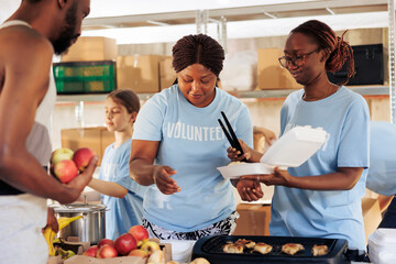 Friendly black women happily serving free food to the poor and needy african american man at a...