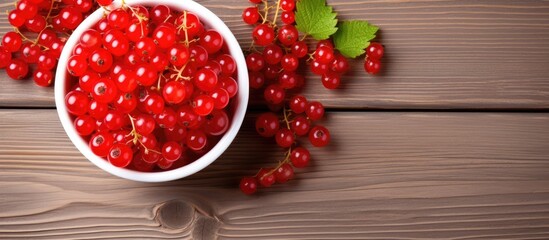 Red currant in a white bowl on a wooden background viewed from above and with empty space