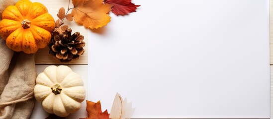 Fototapeta premium Fall themed flat lay with empty paper and dried leaves alongside a pumpkin on a table Copy space