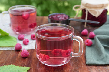 Fresh raspberry tea, berries and jars of jam on wooden table. Vitamin C drink. Anti-cold tea is an antioxidant for health in the flu season of colds. Side view.

