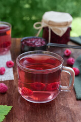 Fresh raspberry tea, berries and jars of jam on dark table. Vitamin C drink. Anti-cold tea is an antioxidant for health in the flu season of colds. Side view.