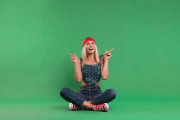 Portrait of happy hippie woman pointing at something on green background