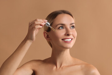 Fototapeta premium Beautiful woman applying cosmetic serum onto her face on beige background