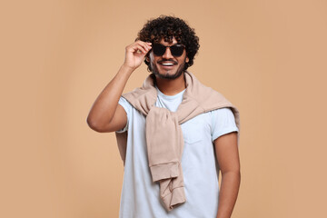 Handsome young smiling man in sunglasses on beige background