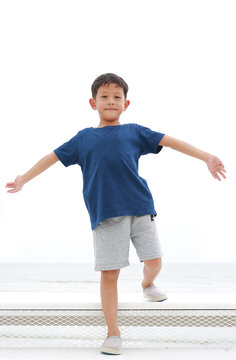Asian little boy arms outstretched or keeping arms raised on white stair at seaside. Child with hands wide open.