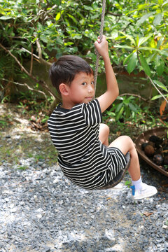 Portrait of Asian little boy kid play sitting hang on swing in the garden.