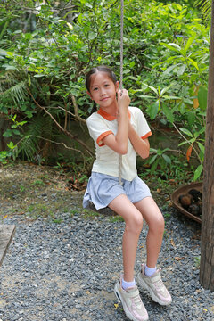Asian girl child play sitting hang on swing in the garden.