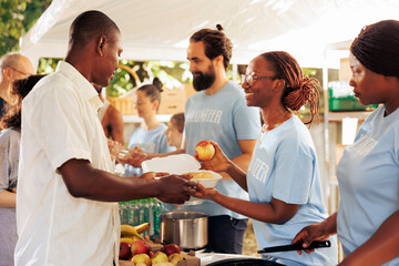 African american and caucasian volunteers handing out free food and necessities to the needy. At homeless shelter friendly charity workers give hunger relief and humanitarian help to less fortunate.