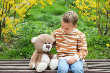 Little girl with teddy bear on wooden bench outdoors