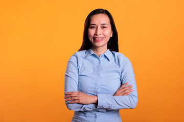 Portrait of smiling woman standing in arm crossed posing in studio over yellow background, smiling at camera during shoot. Cheerful filipino model with joyful expression having fun, enjoying free time