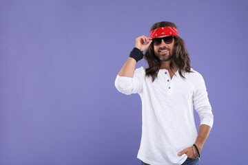Stylish hippie man in sunglasses on violet background, space for text
