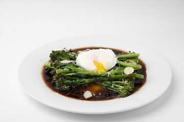 Tasty cooked broccolini with poached egg, almonds and sauce on white background, closeup