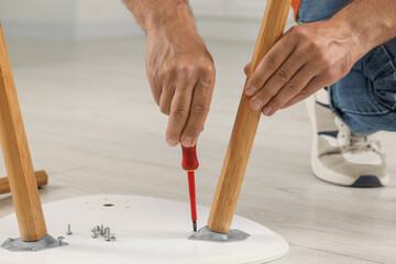 Man with screwdriver assembling furniture on floor indoors, closeup