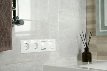 Light switches and power sockets on light grey wall in bathroom. Space for text