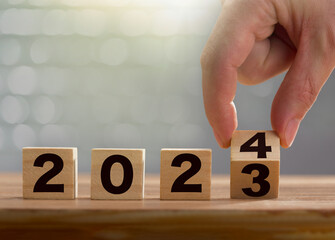 Start of the new year 2024. Business man hand flips wooden cubes with 2023 to 2024 on shiny background. Happy new year, new business, plan, goals, strategy concept. Aniversary time. 