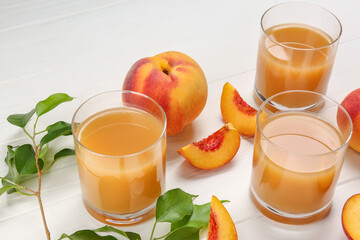 Glasses of peach juice, fresh fruits and leaves on white wooden table