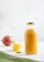 Bottle of fresh mango smoothie with pieces on light background.