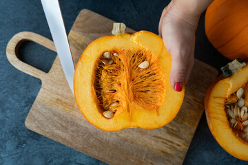 Woman cutting pumpkin into slices with a knife. Fresh raw sliced pumpkins pieces. Preparing ingredients for a seasonal autumn fall dish, soup or pie.