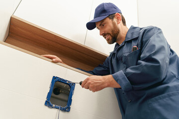 Repairman holding screwdriver tool while installing toilet flush panel in apartment under renovation
