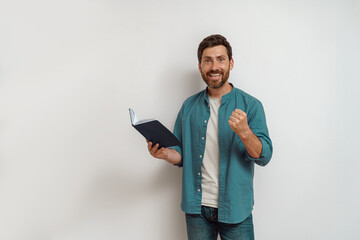 Smiling male freelancer in casual clothes standing with open notepad on white background