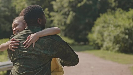 Happy little girl running towards African American father in military camouflage uniform, hugging him and smiling while meeting after returning home on summer day - Powered by Adobe