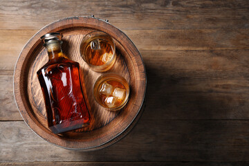 Barrel, bottle and glasses of tasty whiskey on wooden table, top view. Space for text