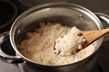 Wooden spoon with delicious rice over pot, closeup