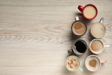Fototapeta na wymiar Many cups with different aromatic coffee on light wooden table, flat lay. Space for text