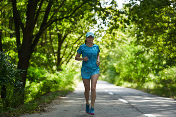 Obraz premium Woman running through forest on asphalt