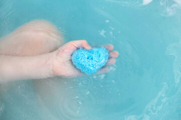 Fototapeta premium Bath bomb blue with coconut extract in the form of a heart in the hand of a child. Cosmetics and skin care. Copy space for text