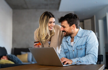 Fototapeta na wymiar Cheerful young couple using laptop and smiling while shopping online at home