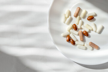 Fototapeta na wymiar Minimal lifestyle aesthetic medicine concept. White and brown pills and capsules on white plate and marble table background with natural sun light shadows