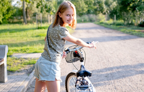 Cute preteen girl with bycicle outdoors looking at camera and smiling. Pretty child with bike at city street at summer portrait