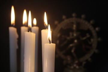 Lit white candles in the dark with blurry Kali goddess statue