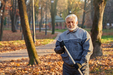 Senior service worker looking at camera, while gathering fallen leaves at daytime. Portrait of...