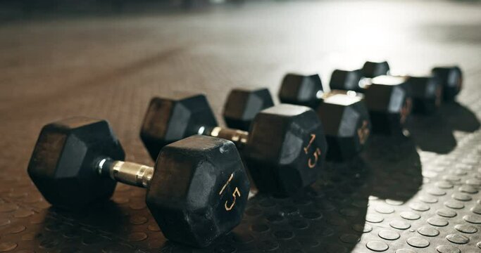 Fitness, background and dumbbells in empty gym for exercise, bodybuilding workout and sports training. Closeup of heavy steel weights, equipment and iron on floor in wellness club for muscle power