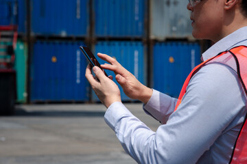 Technology concept, A man, shipping worker touching smart phone screen to manage an online order at the container dock, stock, freight and cargo supply chain logistics