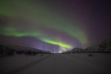 Violet and green Northern lights over dark winter road