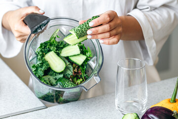 A woman with blender chopping cucumber for smoothie at home.