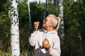 Young blonde girl with boletus mushrooms in the forest on an autumn day.