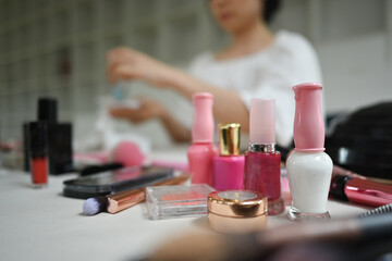 Various makeup products on dressing table with female beauty blogger recording video in background