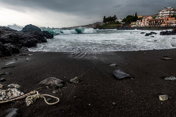Waves hitting the shore on a cloudy overcast rainy stormy day. Cyclops Coast, black volcanic rocks and send on Sicily, near the town of Acireale