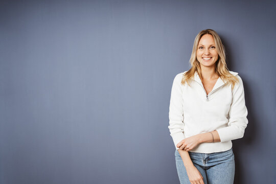 Smiling Young Woman in White Sweater Standing Against Blue Wall with Copy Space