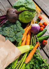 Colorful vegetables in a brown paper shopping bag on a wooden table. Different vegetables on the table made of dark wood. Raw vegetables from the store. Products in a paper eco-bag. Selective focus.
