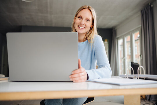 Smiling Young Blonde Woman Working in an Office with a Laptop and Looking at the Camera