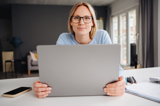Young Blonde Woman with Glasses Looking at the Camera Over Her Laptop