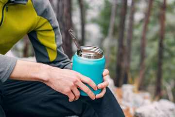 Embracing nature's flavors: A hiker enjoys a hot breakfast, holding a thermos amid a serene outdoor...