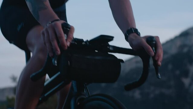 Cinematic close up on man riding professional road bike with spinning rotors, water bidon bottle, clipped in pedals, handlebar bag, cycling computer and helmet. Carbon road bike and athlete in dusk