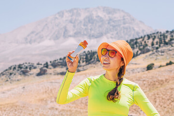 Pretty young woman biting on a energy sportive gel drink after a good hike in high mountains